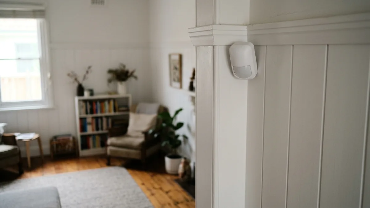 Small white wireless PIR motion sensor mounted high in the corner of a room in a Sydney home