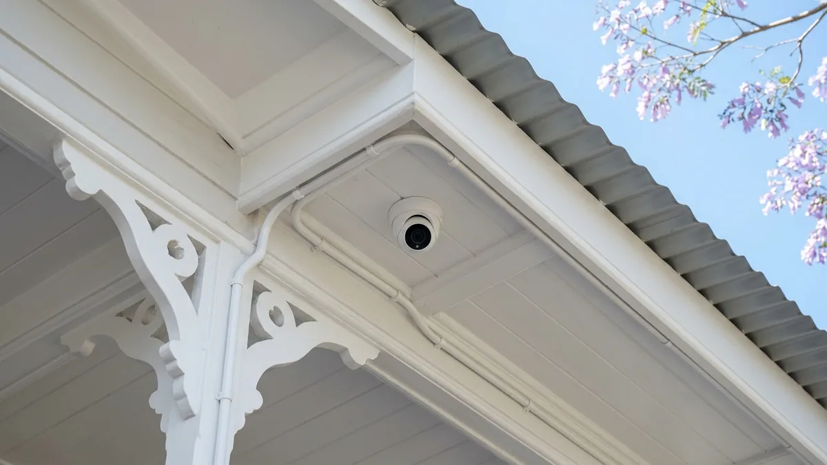 A white CCTV dome camera tucked neatly under the timber eave of a Brisbane Queenslander, with cabling run tidily along the fretwork soffit.